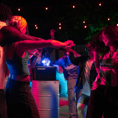 People dancing around a soundboks go with a lightboks on top with colorful lights at a party.